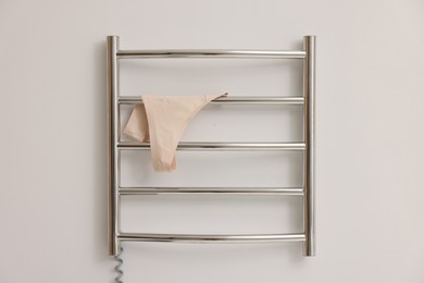 Photo of Heated towel rail with beige underwear on white wall