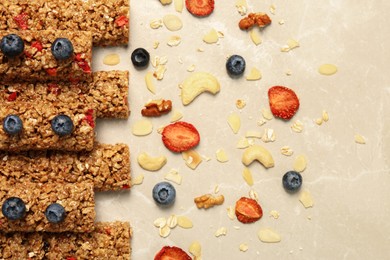 Photo of Tasty granola bars, blueberries, dried strawberries and nuts on beige marble table, flat lay
