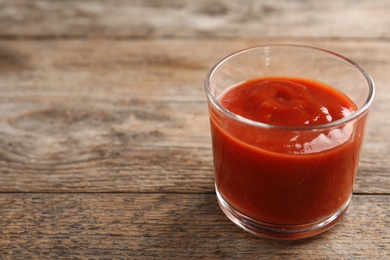 Photo of Glass of tasty tomato sauce on wooden table. Space for text