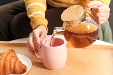 Photo of Woman pouring aromatic tea into cup at table, closeup