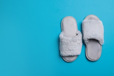Photo of Pair of soft fluffy slippers on blue background, top view. Space for text