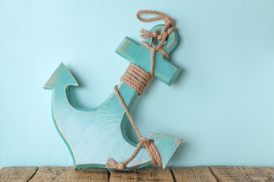 Photo of Anchor with hemp rope on wooden table near turquoise wall