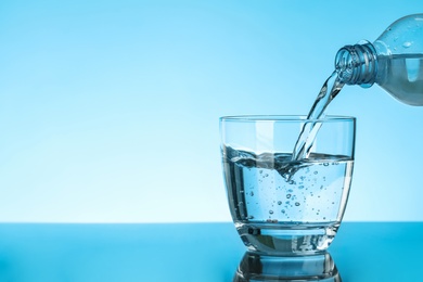 Photo of Pouring water from bottle into glass on blue background, space for text. Refreshing drink