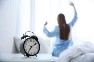 Young woman stretching at home in morning, focus on alarm clock