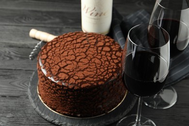 Photo of Delicious chocolate truffle cake, red wine and corkscrew on black wooden table
