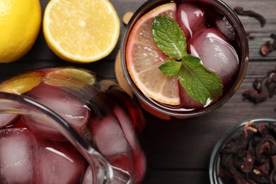 Refreshing hibiscus tea with ice cubes, lemon and mint on wooden table, flat lay