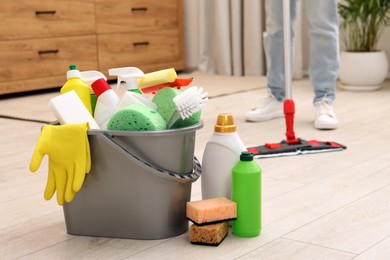 Photo of Different cleaning supplies in bucket and woman mopping floor, selective focus