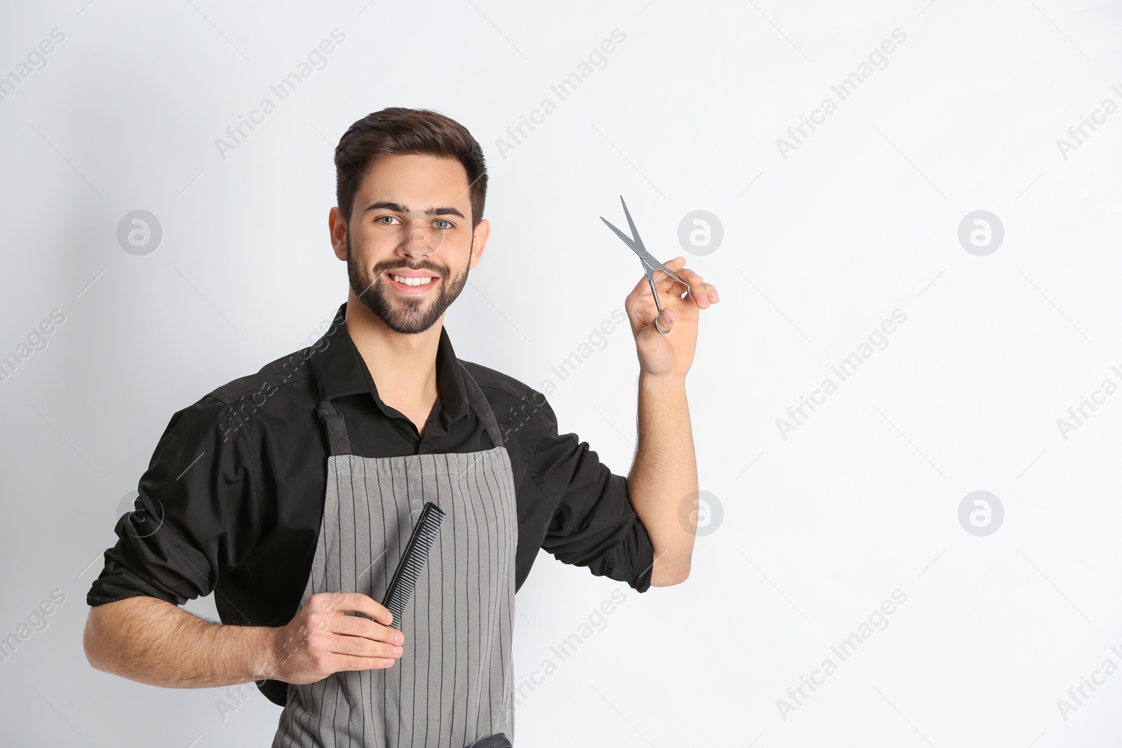 Photo of Young hairstylist holding professional scissors and comb on light background