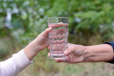 Child giving glass of water to elderly woman outdoors, closeup