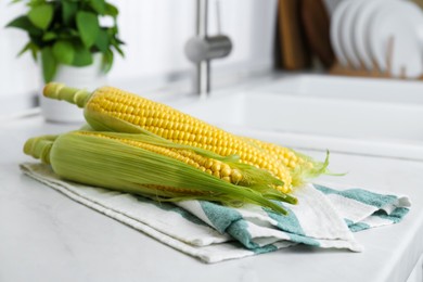 Photo of Tasty sweet corn cobs on white countertop in kitchen