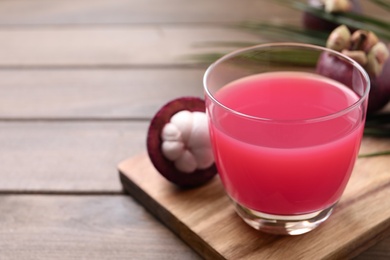 Delicious fresh mangosteen juice in glass on wooden table, space for text