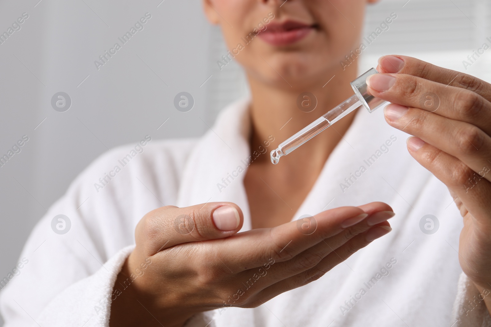 Photo of Woman applying cosmetic serum onto her hand on light background, closeup