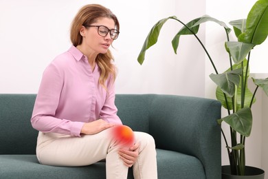 Image of Arthritis symptoms. Woman suffering from knee pain on sofa indoors