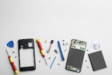 Photo of Disassembled mobile phone and repair tools on light background, flat lay