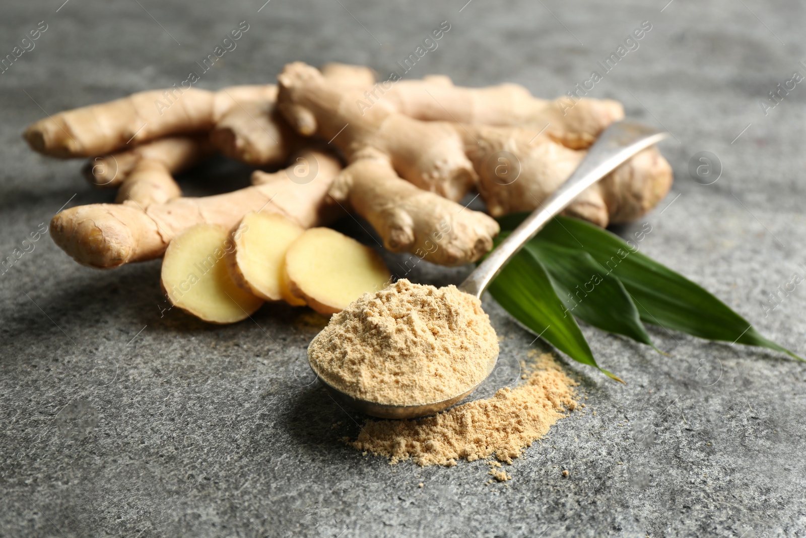 Photo of Dry ginger powder, fresh root and leaves on grey table