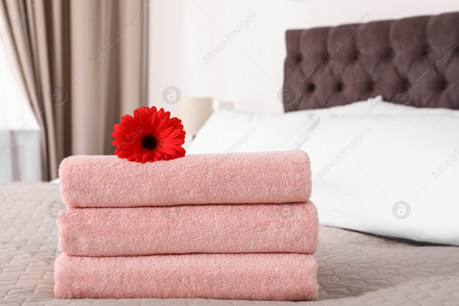 Photo of Stack of fresh towels with flower on blanket in bedroom. Space for text
