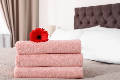 Stack of fresh towels with flower on blanket in bedroom. Space for text