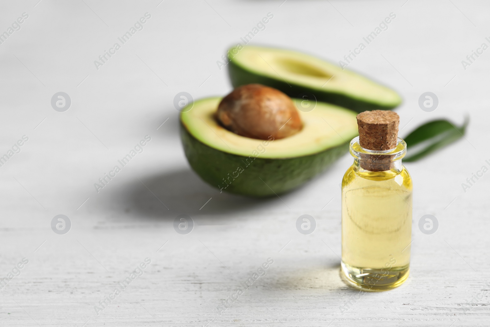 Photo of Bottle with oil and fresh avocado on wooden table