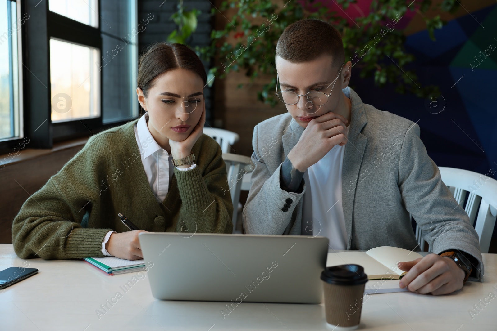 Photo of Young students with laptop studying at table in cafe