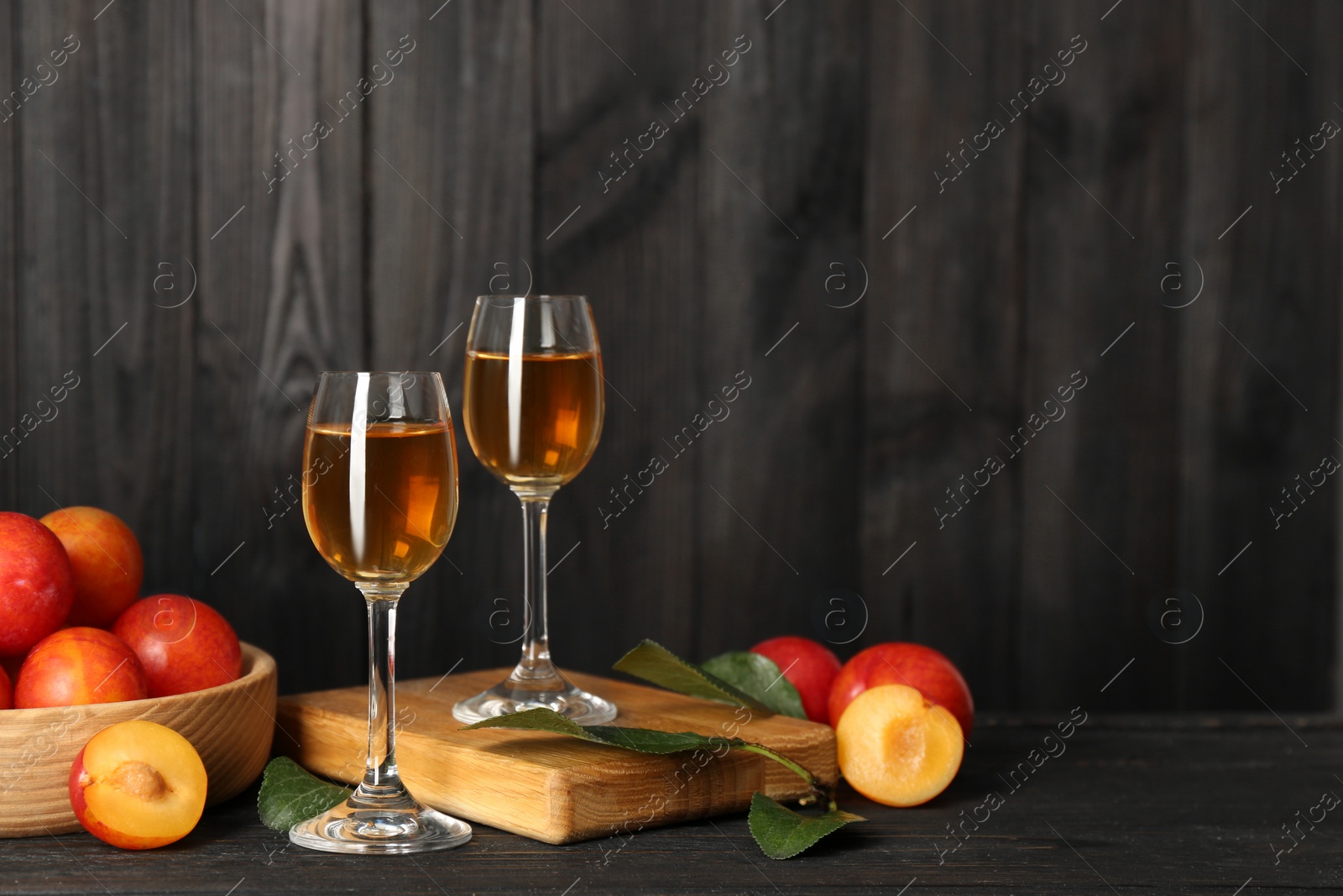 Photo of Delicious plum liquor and ripe fruits on black wooden table. Homemade strong alcoholic beverage