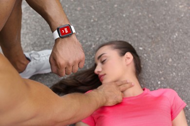 Image of SOS function. Man sending emergency call via smartwatch while checking woman's pulse outdoors, closeup