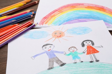 Photo of Cute child`s drawings and colorful pencils on wooden table