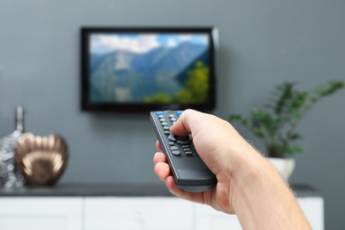 Image of Man switching channels on TV set with remote control at home