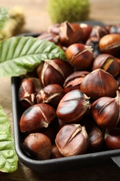 Photo of Delicious roasted edible chestnuts and green leaves on wooden table, closeup