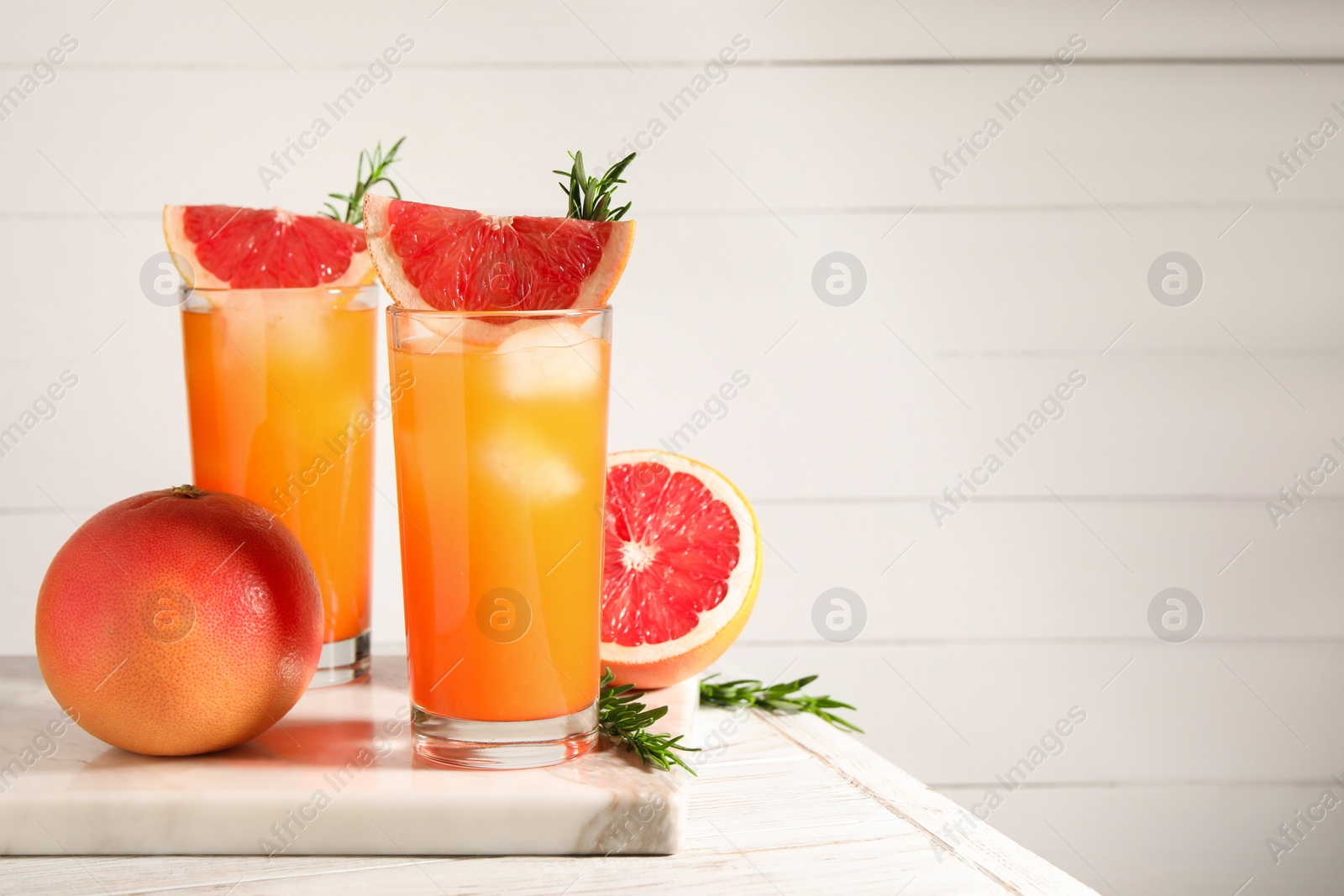 Photo of Tasty grapefruit drink with ice in glasses, rosemary and fresh fruits on light wooden table. Space for text
