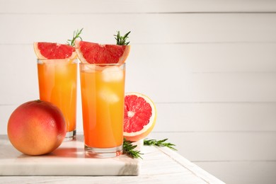 Photo of Tasty grapefruit drink with ice in glasses, rosemary and fresh fruits on light wooden table. Space for text