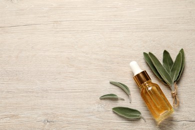 Photo of Bottle of essential sage oil and plant leaves on wooden table, flat lay. Space for text