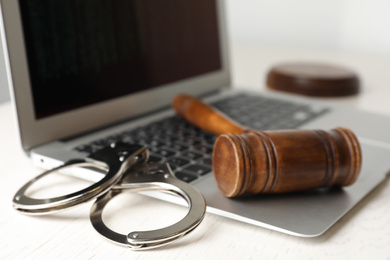 Photo of Laptop, gavel and handcuffs on white table, closeup. Cyber crime