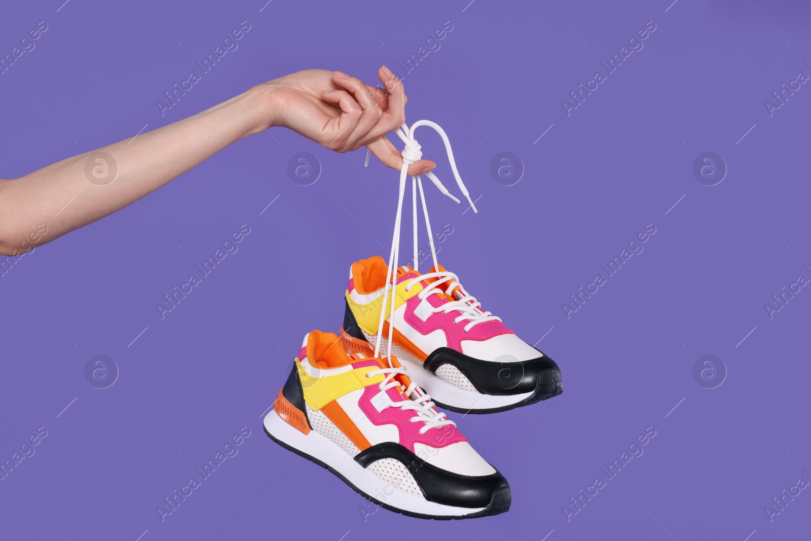 Photo of Woman holding pair of stylish colorful sneakers on purple background, closeup