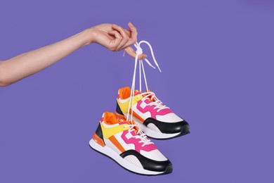 Woman holding pair of stylish colorful sneakers on purple background, closeup