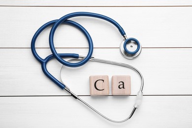 Photo of Cubes with symbol Ca (Calcium) and stethoscope on white wooden table, top view