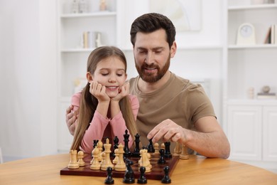 Father teaching his daughter to play chess at home