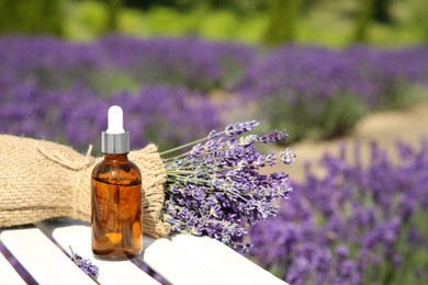 Bottle of essential oil and lavender flowers on white wooden surface outdoors, space for text