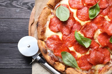 Tasty pepperoni pizza with basil and cutter on black wooden table, top view