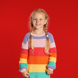 Cute little girl in warm sweater on red background. Winter season