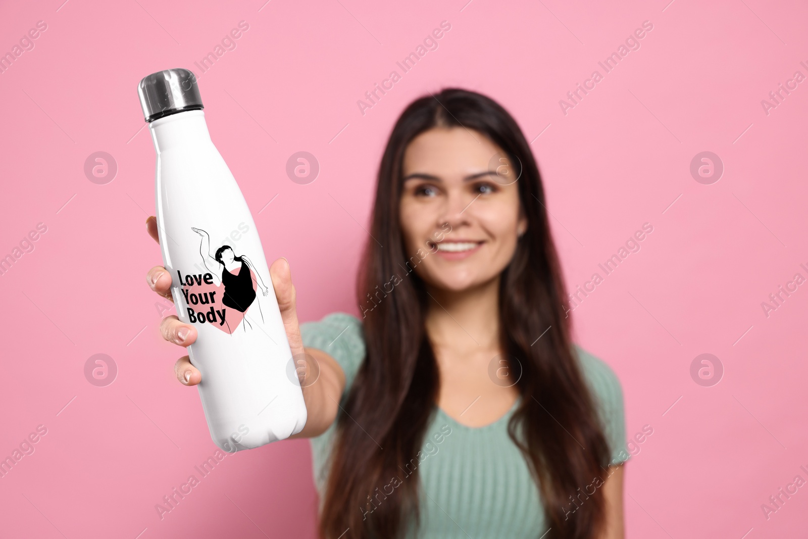 Image of Smiling woman holding thermo bottle with drawn figure of plus-size model, heart and phrase Love Your Body against pink background, selective focus