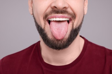 Happy man showing his tongue on light grey background, closeup