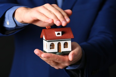 Photo of Male agent covering house model, closeup. Home insurance