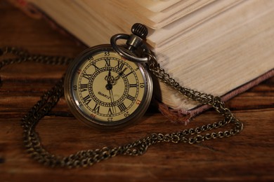 Photo of Pocket clock with chain and book on wooden table, closeup