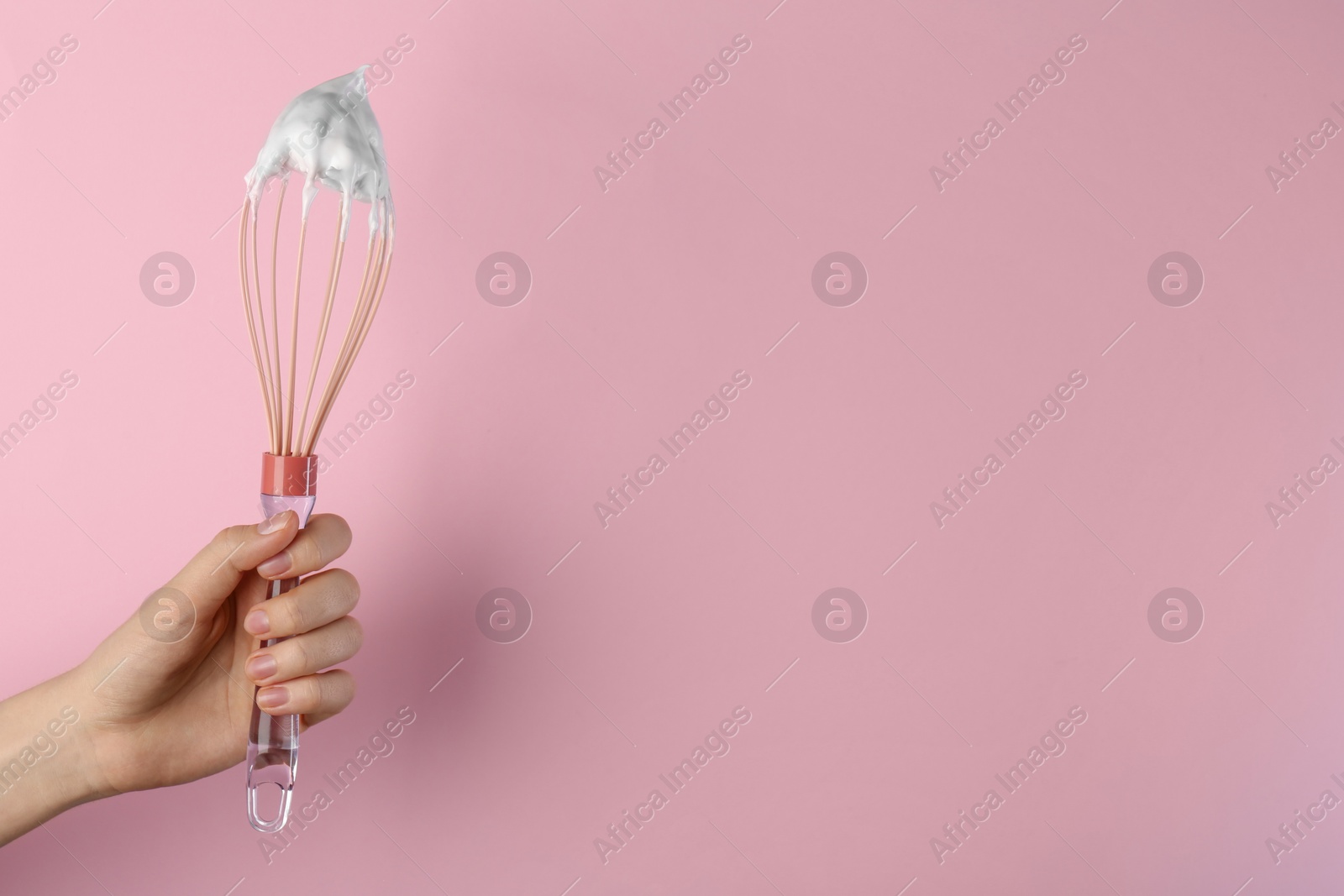 Photo of Woman holding whisk with whipped cream on pink background, closeup. Space for text