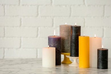 Photo of Different decorative wax candles on table against brick wall