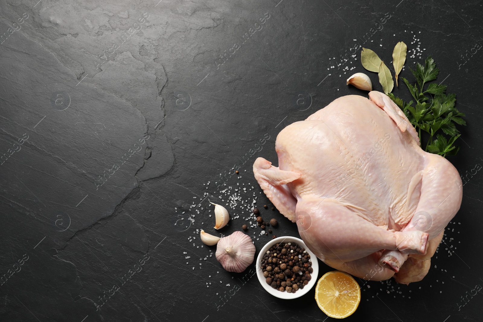 Photo of Fresh raw chicken with spices and lemon on black textured table, flat lay. Space for text