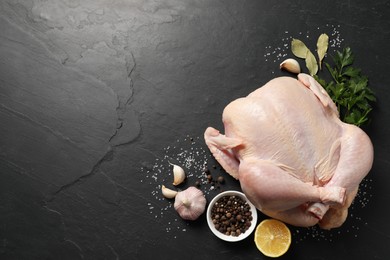 Photo of Fresh raw chicken with spices and lemon on black textured table, flat lay. Space for text