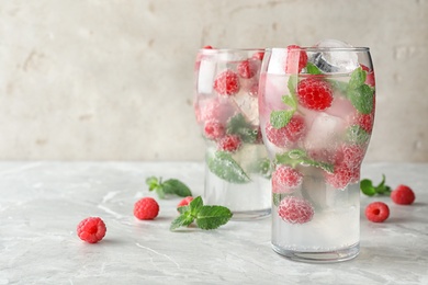 Photo of Glasses of refreshing drink with raspberry and mint on grey stone table, space for text