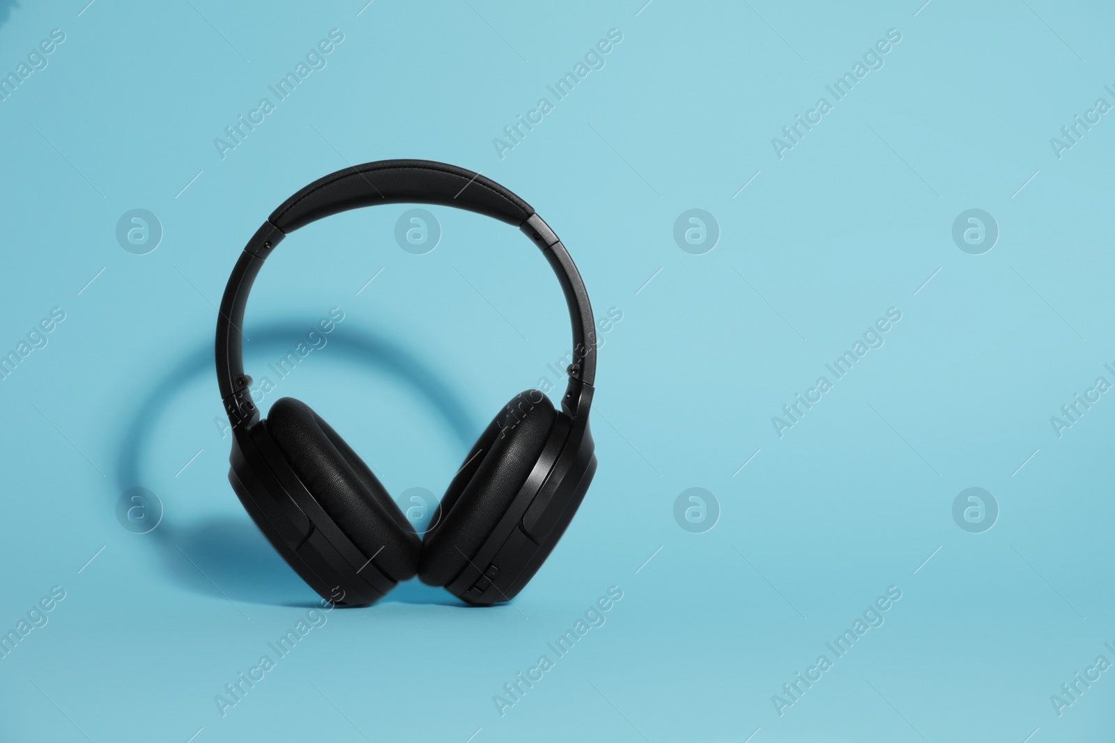 Photo of Modern wireless headphones on light blue background. Space for text