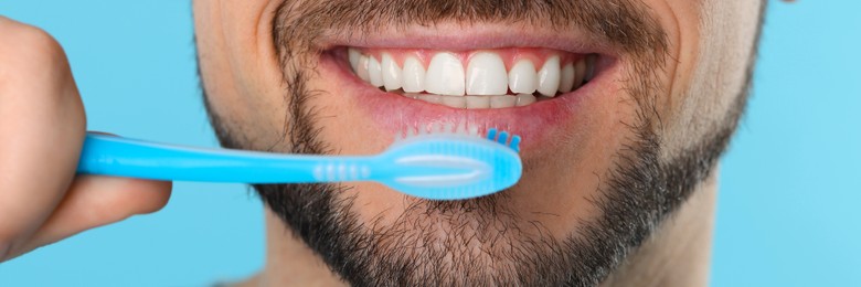 Image of Man brushing his teeth with plastic toothbrush on light blue background, closeup. Banner design